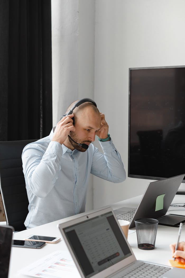 gallery-03 A bald male call center agent adjusting his headset during work in a modern office setting.